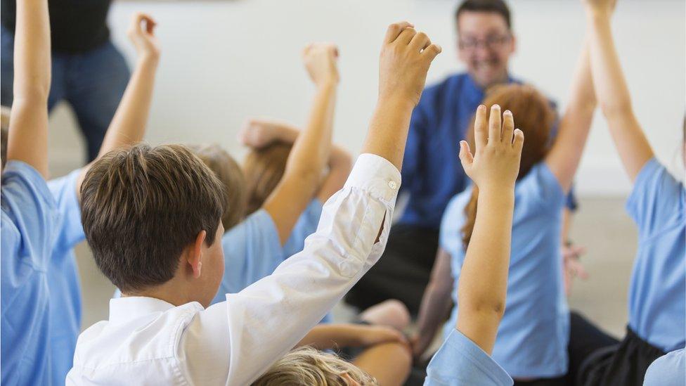 Excited school children in school uniform with hands up ready to answer a question from the teacher