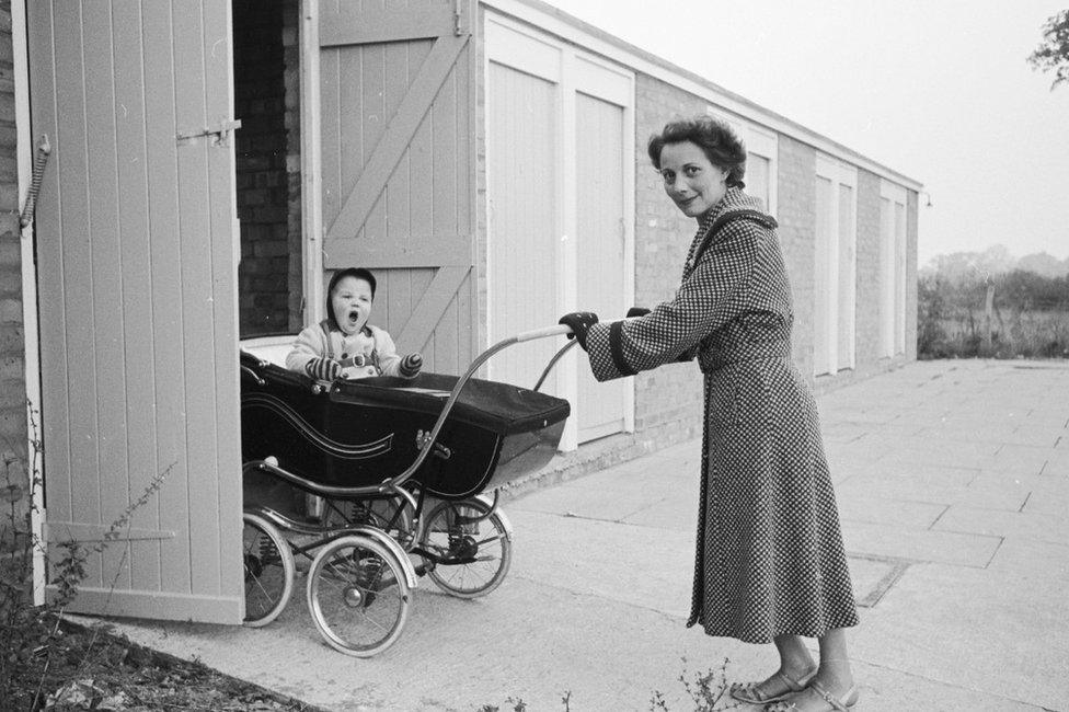 1955: A mother pushing her baby in its pram into a pram garage in Harlow, where one-fifth of the population is under five years old.