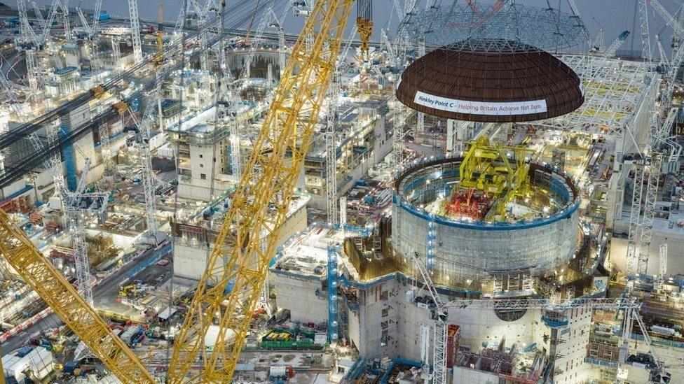 A huge industrial nuclear reactor, still in it's construction phase. There are large yellow cranes lifting the structure into place, and lots of white lights illuminating the area. 