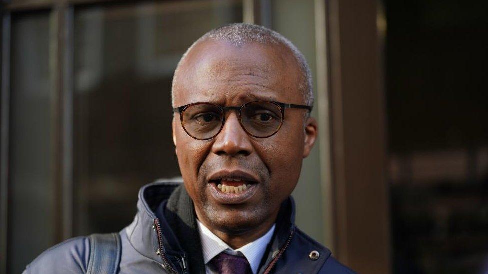 Man with very short hair and glasses stands outside office building