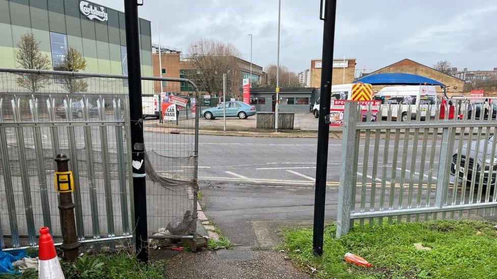 Gap in metal fencing between busy road and footpath