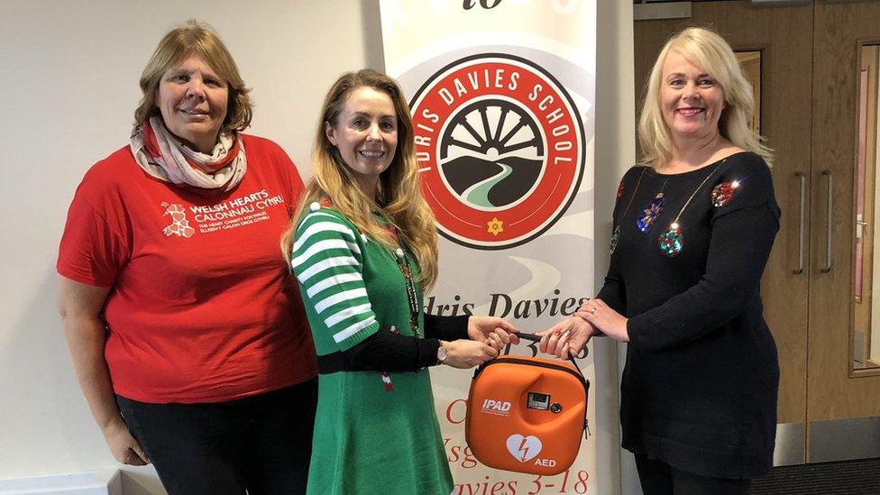 A defibrillator presentation at Idris Davies School. There are three women in the photograph. The second and third are passing a defribilator to one another).