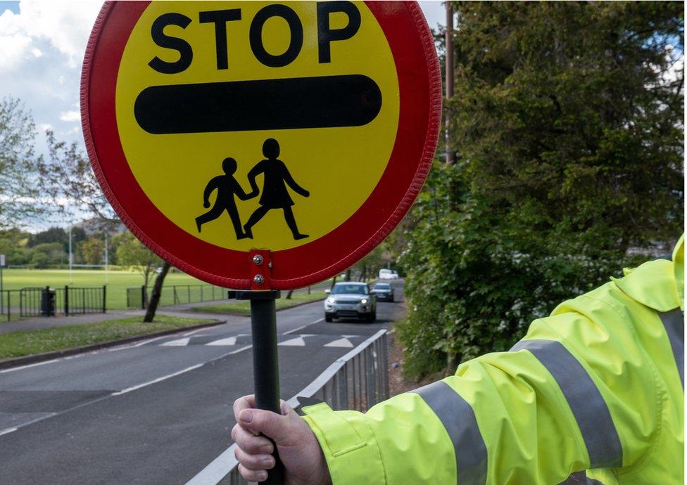 The arm of a crossing guard, known as a lollipop man or lady in the UK, preparing to stop traffic so school children can cross the road safely.