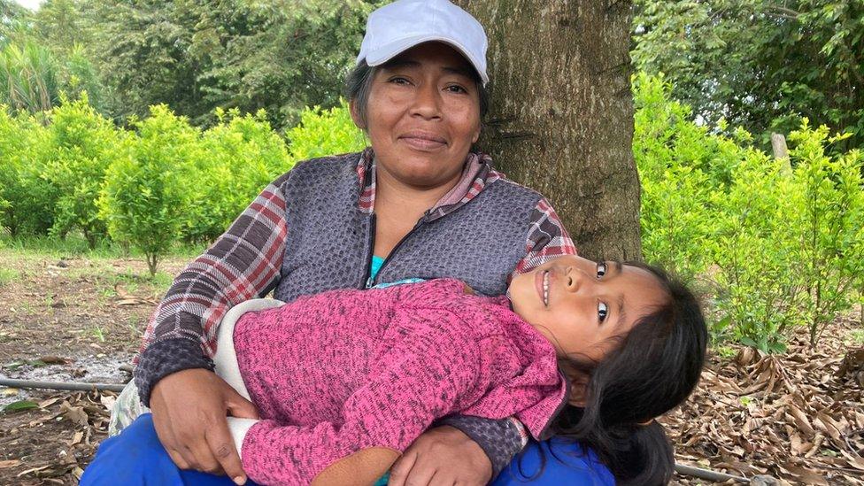 Farmer Irma sitting under a tree holding a child