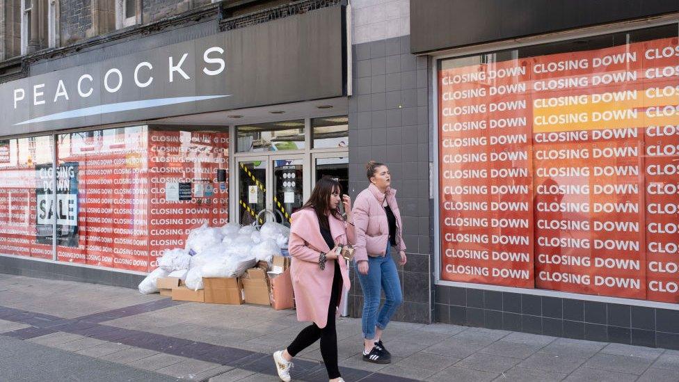 Two young women walk past a closed Peacocks clothing store on Bangor High Street