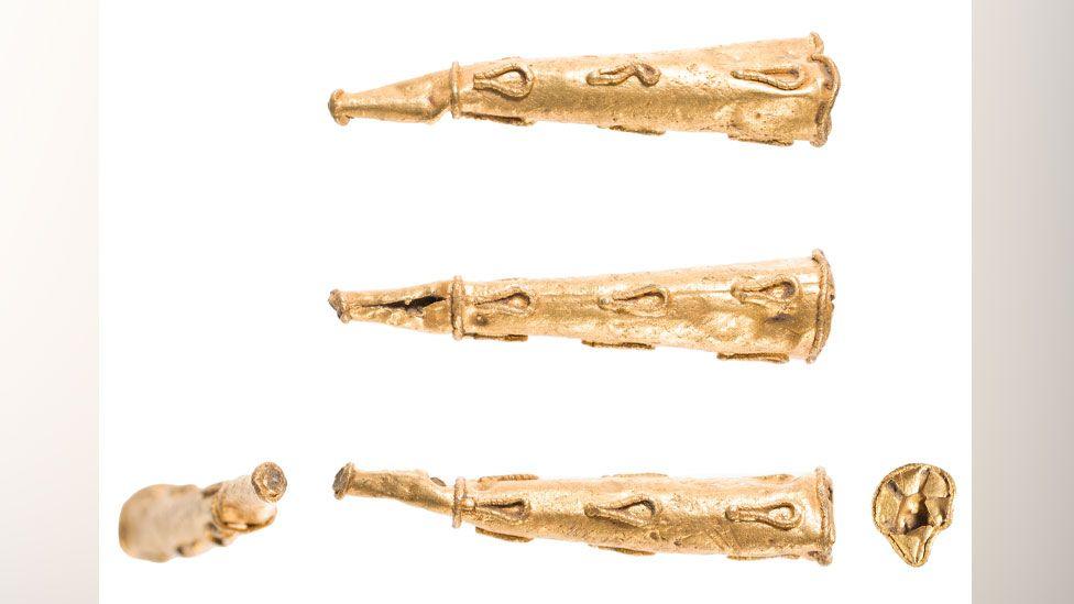 Five views of the same Roman earring. It is conical in shape and made from gold. Three of the views show it on its side, with the narrowest end on the left and the wider end on the right. The ring has trim soldered around its circumference at top and bottom, as well as about a quarter of the way down from its narrowest end. More trim is soldered in loops on its side. The last two views have the camera focused on its tip and on its base 