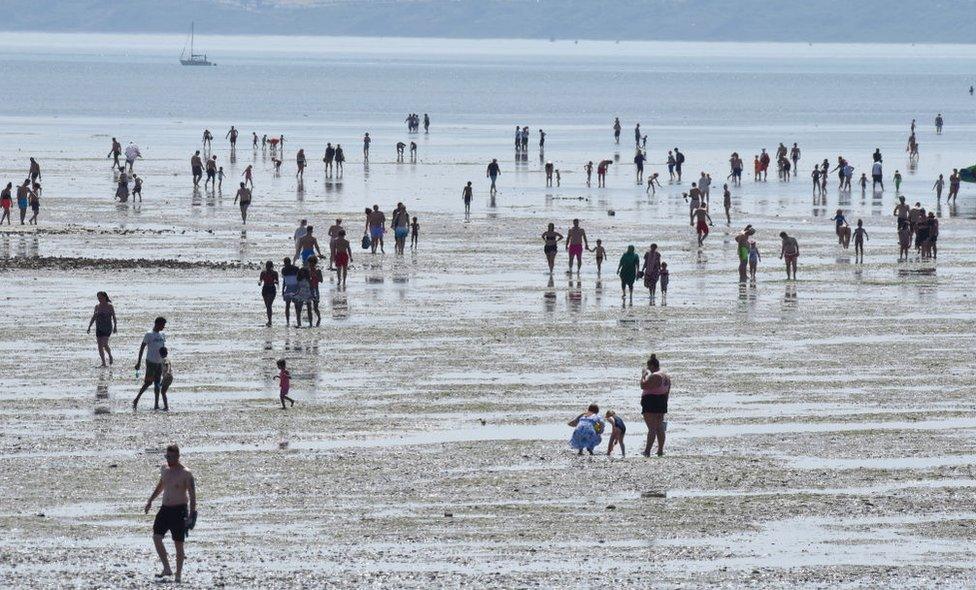 People walk out at low tide into the sea as they gather to enjoy the warm sunny weather on Jubilee beach on July 18, 2021 in Southend-on-sea, England.