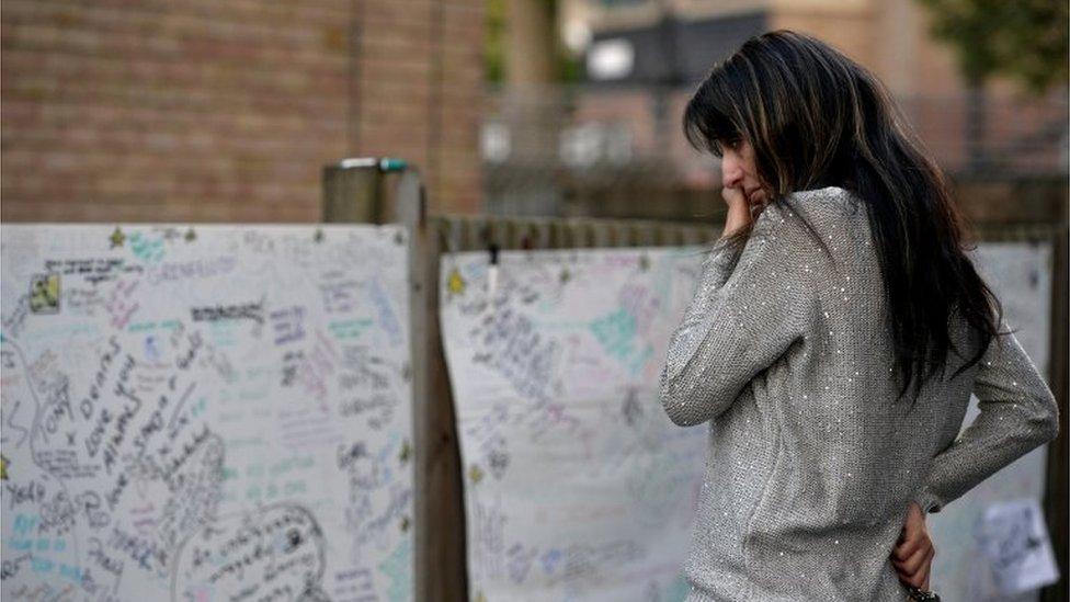 A woman reacts in front of a message wall near the scene of the fire that destroyed the Grenfell Tower block