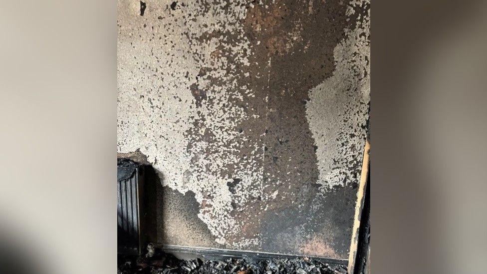 A photograph that shows the fire-damaged wall in the room at the property