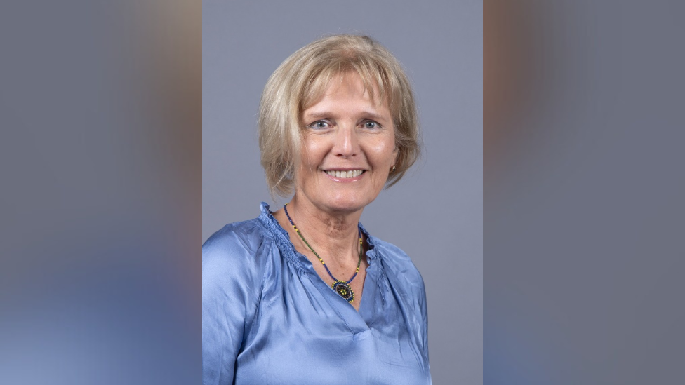 A smiling Rita Horvath looking directly at the camera, wearing a blue silk blouse and necklace. 