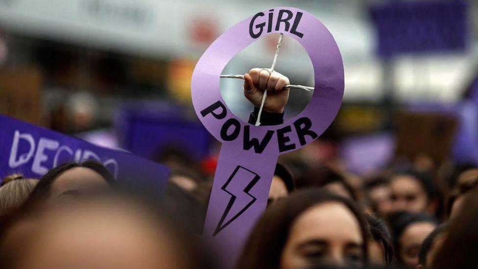 A person holds up a sign that reads 'girl power'