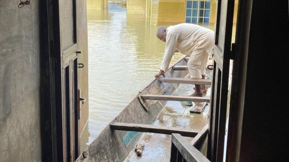 Mohammed Sani Gambo stands in a canoe. Its front is moored inside the doorway of his flooded house.