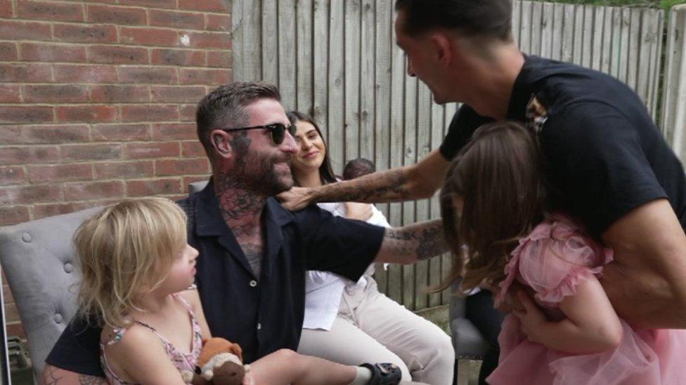 The dads hug, with their daughters on their laps