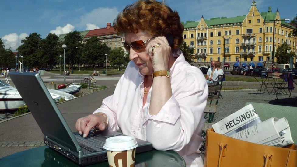 A woman talks on a phone and works on a laptop outside in Helsinki