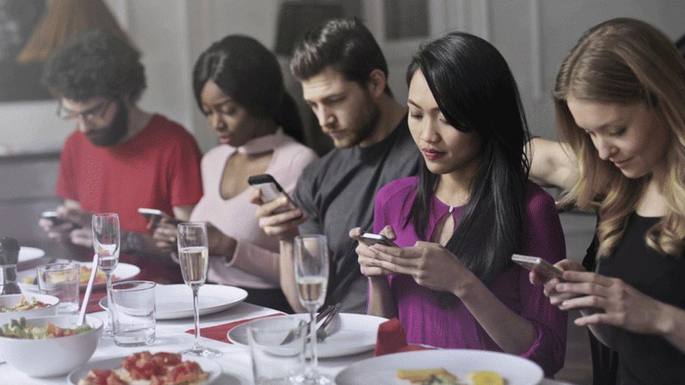 Group of adults sit at dinner on mobile phones