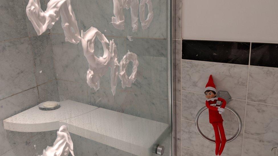 An elf on a towel holder next to a shower screen covered in shaving foam