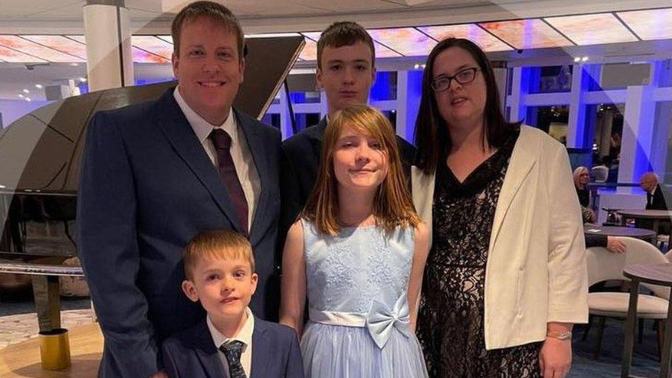 family of five - a wife, husband, two boys and a girl - stand together in formal dress