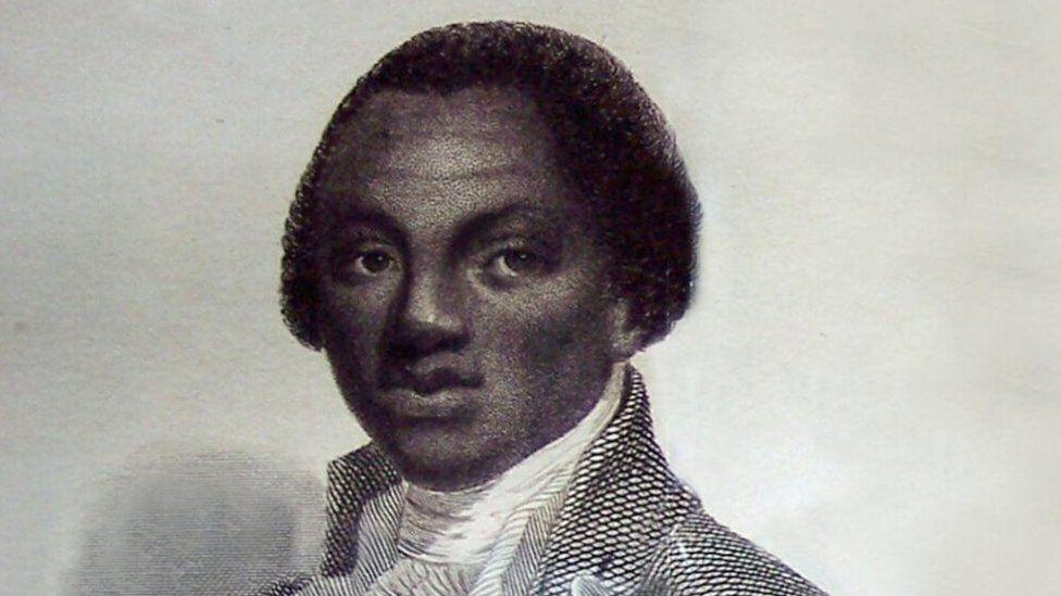 Olaudah Equiano is seen in a black and white photo of a painting. He has short dark hair and is wearing a shirt with a high neck and a jacket