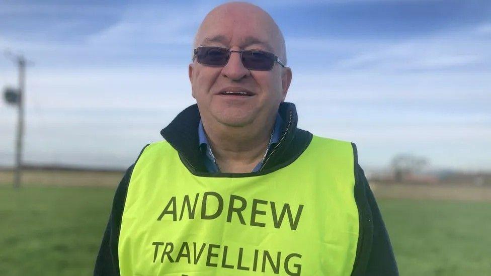 Andrew Elliker-Reeve wearing dark glasses and a yellow-coloured vest with the words "Andrew Travelling Blind" written on the front