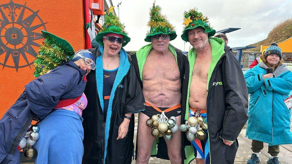 Two women and two men in green hats with tinsel. The men have baubles around their waists