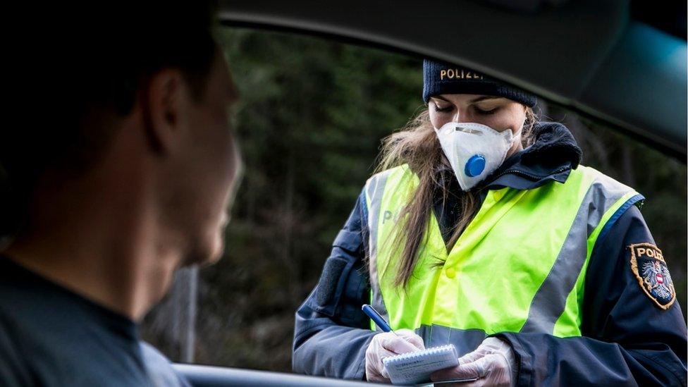 A police officer at a roadblock asks the driver of a car driving out of the Panznautal valley for a drive through permission following the imposition of a quarantine due to the coronavirus on March 14, 2020 near Ischgl, Austria