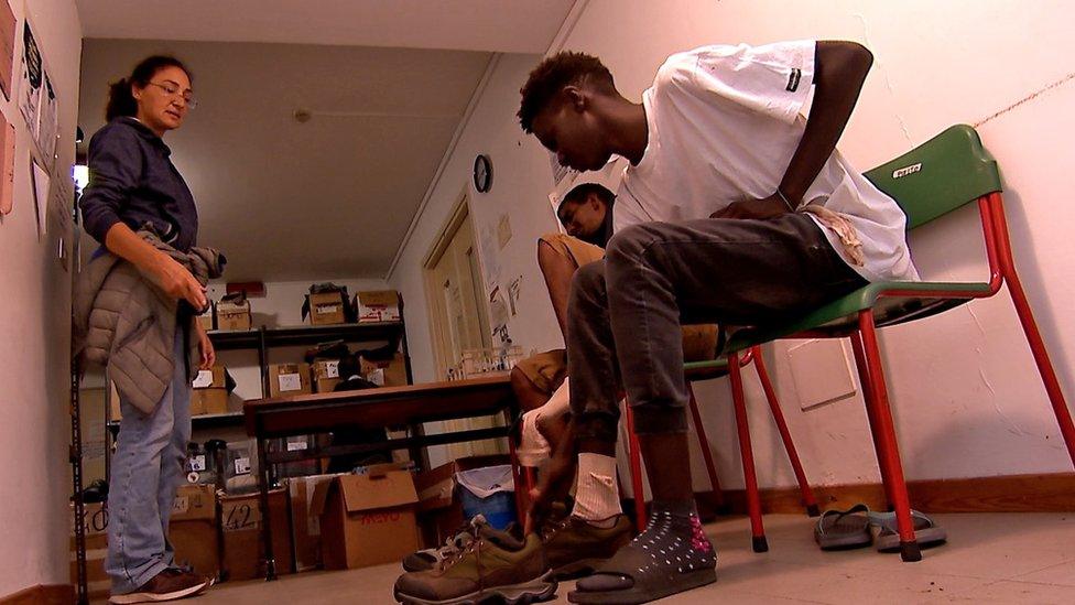 Young men are seen trying on hiking boots at a centre in Oulx in the Italian Alps