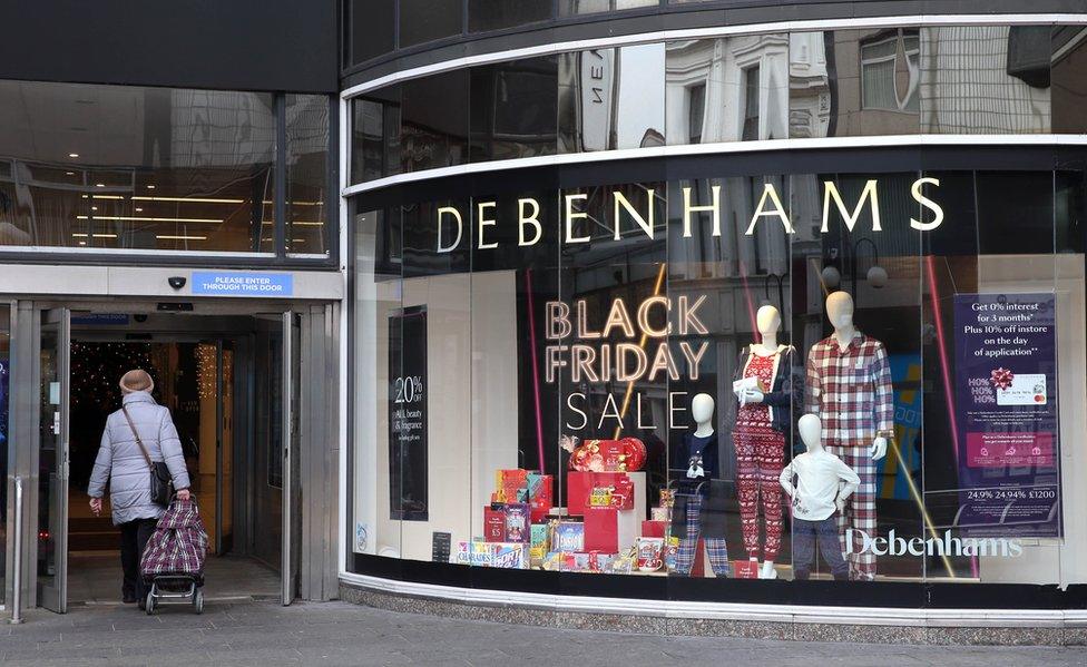 A woman walks past a window of the Debenhams shop in Belfast