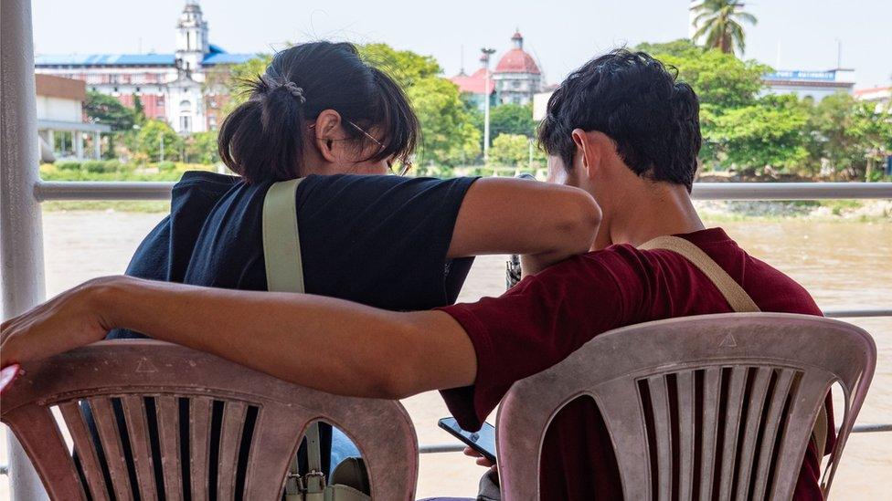 A man and a woman sit next to each other talking, turned away from the camera