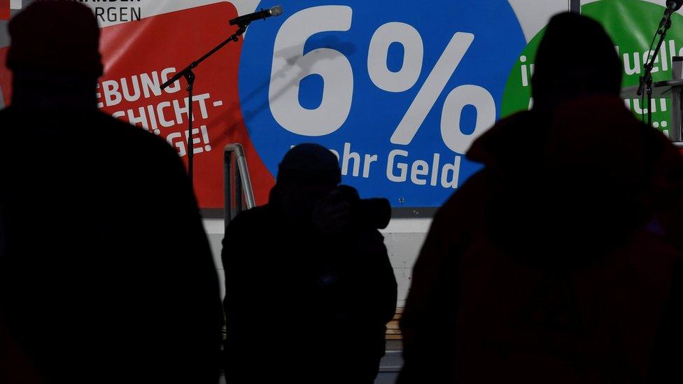 Workers of Airbus stand in front of a banner which reads "6% more money"