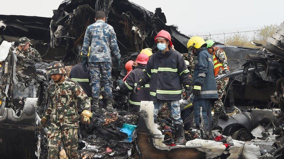 Nepali rescue workers gather around the debris of an airplane