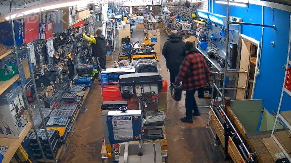 Man on left reaching for tools from display and two men on right walking out of store room with items at Mackays, Cambridge