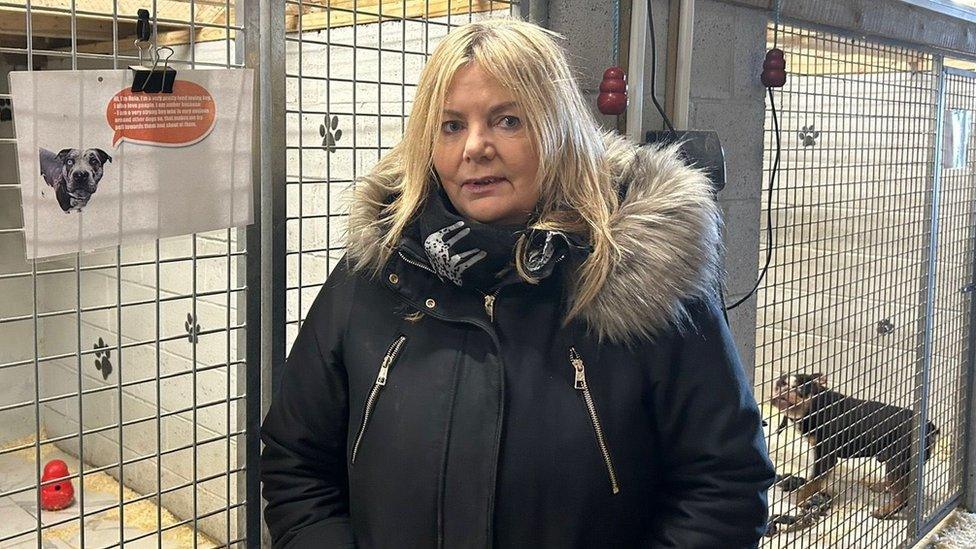 A woman stands in front of a metal dog kennel