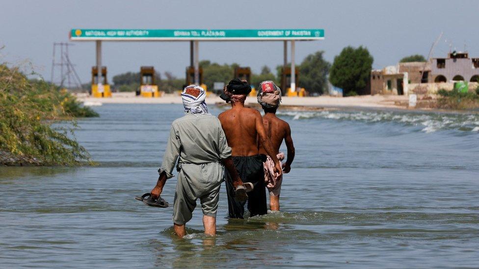 Displaced people walk on flooded highway, following rains and floods during the monsoon season in Sehwan, Pakistan