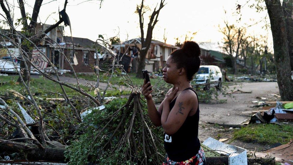 A woman films damage to homes following a tornado strike