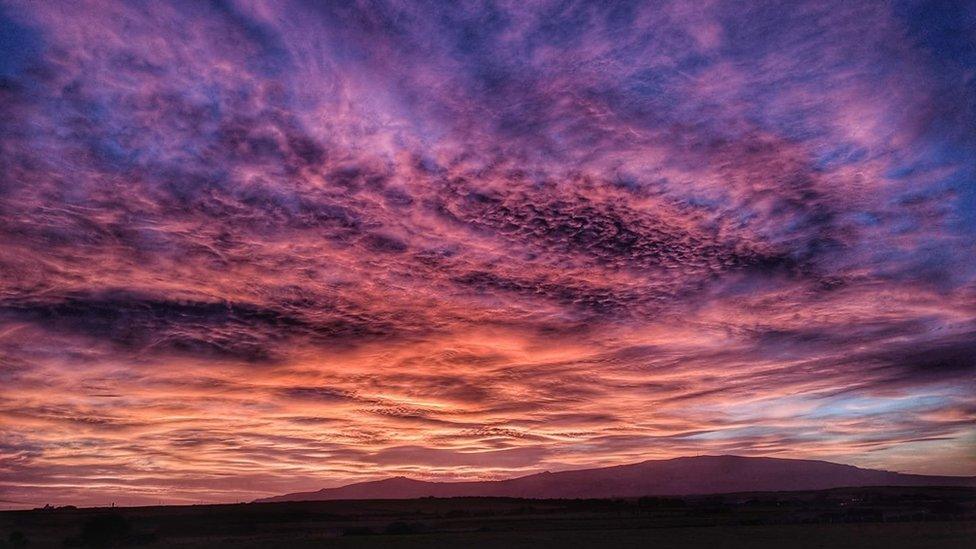 Cymylau fel môr coch uwch ben amlinell mynydd Rhiw