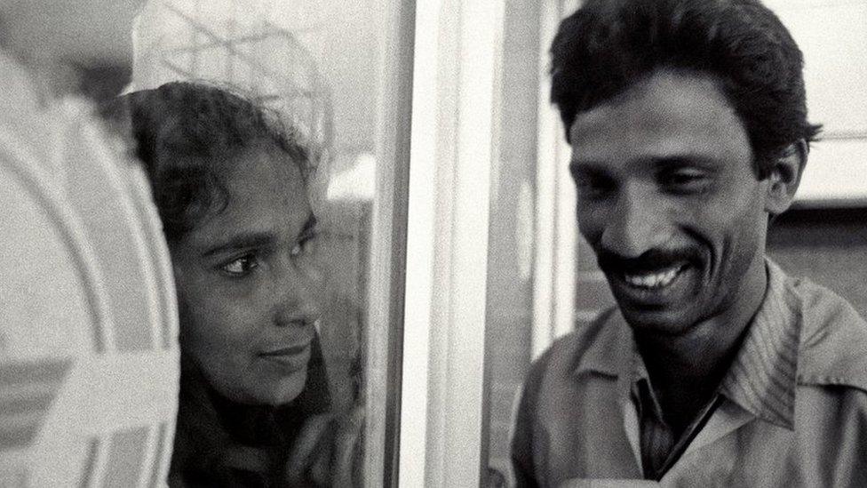 A woman looks at her husband through a window at Dhaka airport