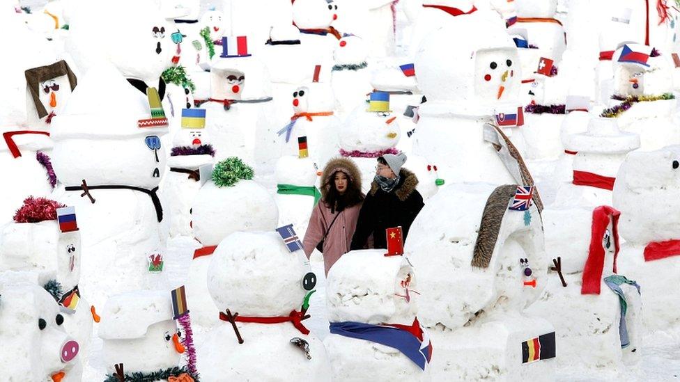 A couple walk between snowmen on Songhua River that displays 2019 snowmen as a part of annual ice festival, in the northern city of Harbin