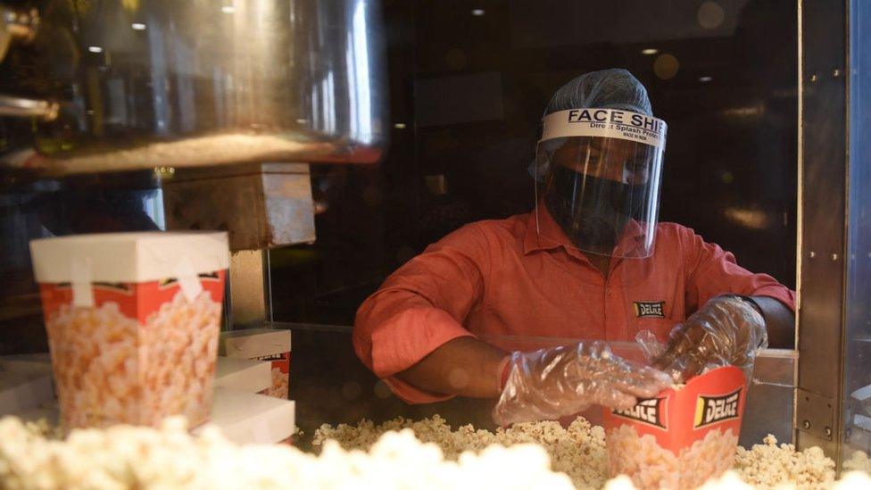 A worker preparing popcorn with health and safety measures after cinemas reopen in India