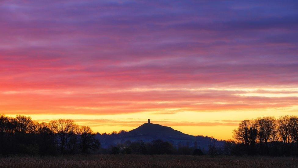 Glastonbury tor in landscape with yellow, red and purple sky