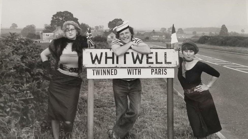 BBC gardening presenter Geoff Hamilton with two other people standing by Whitwell's twin town sign