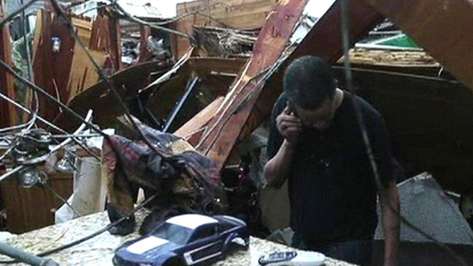 Householder standing amongst tornado debris