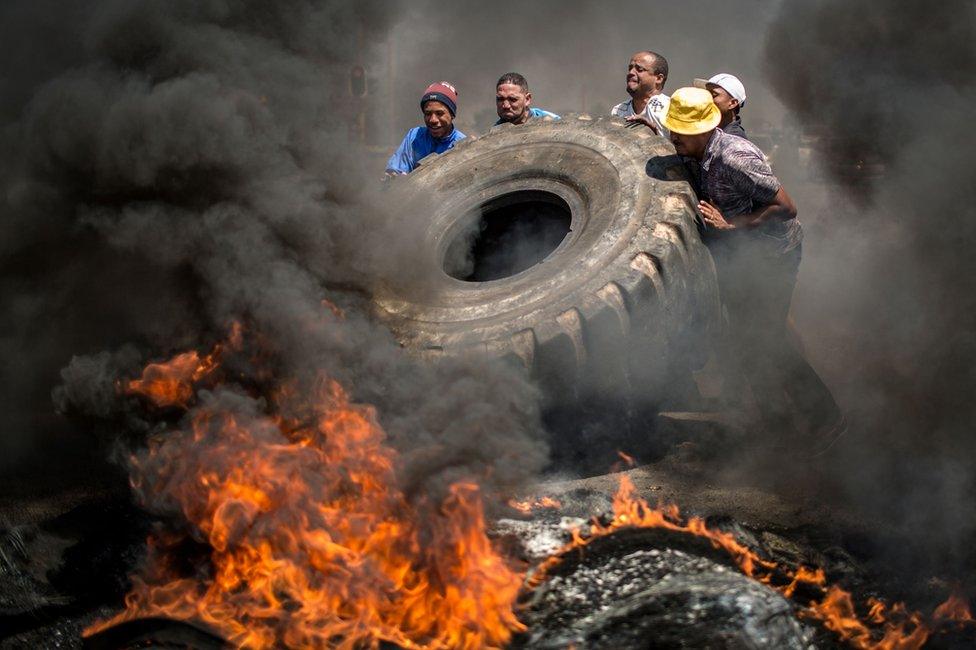 Five men push a giant tyre on to flames