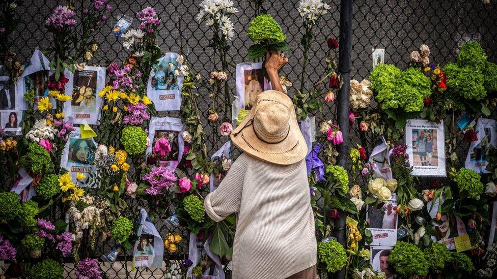 A woman adds flowers to a memorial outside Champlain Tower