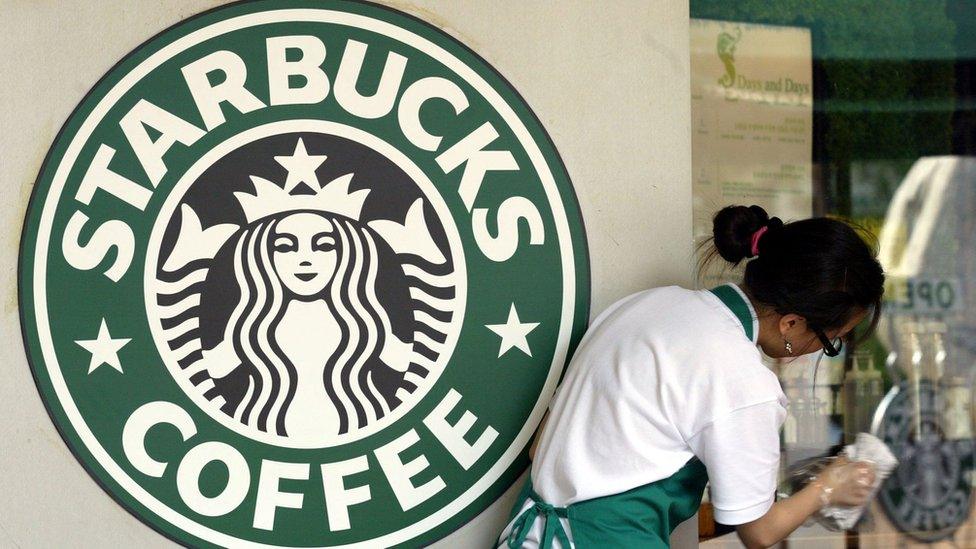 A Starbucks worker making coffee next to the logo