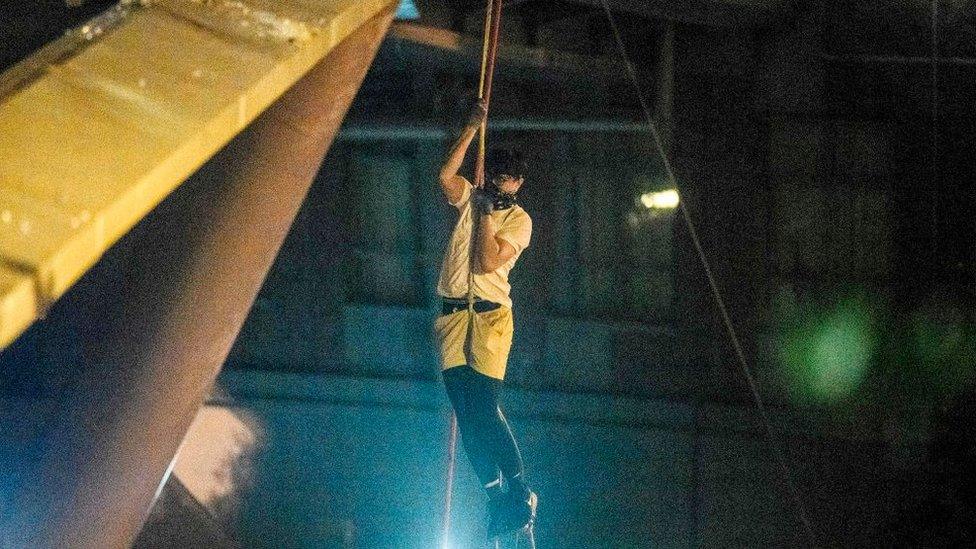 A protester lowers himself down a rope from a bridge to a highway