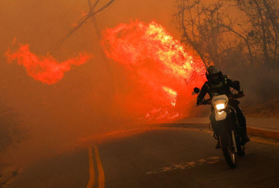 A transit agent rides a motorcycle as a wildfire burns, in Quito, Ecuador September 24, 2024. 