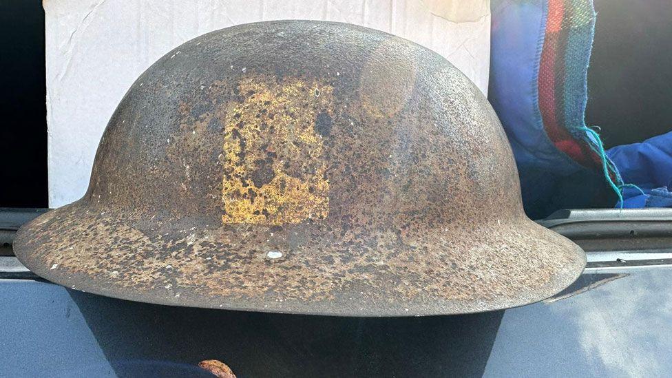 A World War One British infantry helmet repurposed for World War Two. It has a rivet on its rim where a new chin strap and lining would have been added. It has a yellow rectangle on its side with bits of black pigment.