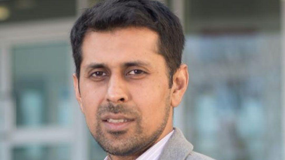 Head shot of councillor Afrasiab Anwar. He has short dark hair and stubble and brown eyes and is wearing a pale grey suit