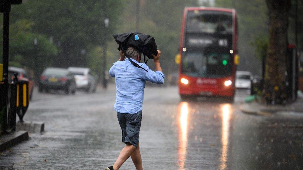 A man in shorts dashes across the road in the pouring rain towards a bus.