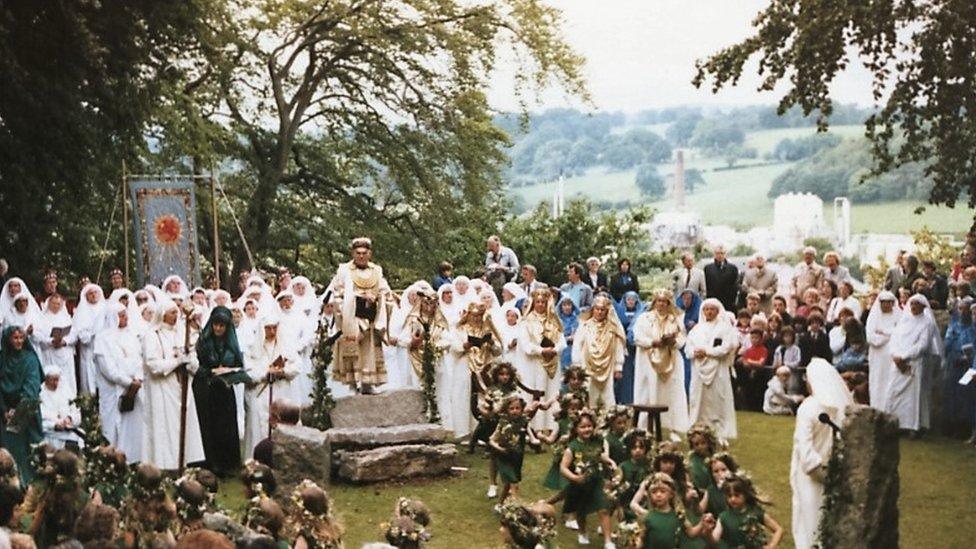 Eisteddfod participants in their robes watched by a big crowd with Synthite factory in the background